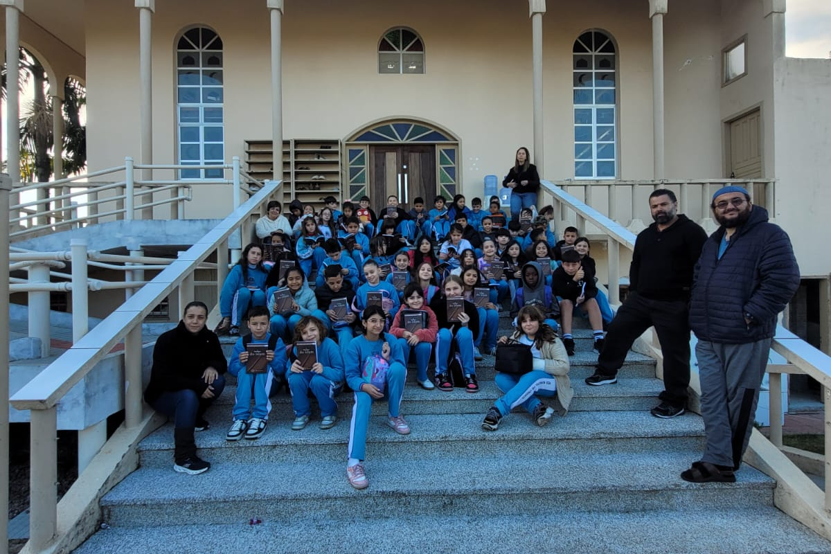 Atividades do MARKAZ - 2026 33 Crianças e educadores reunidos na escadaria com livros