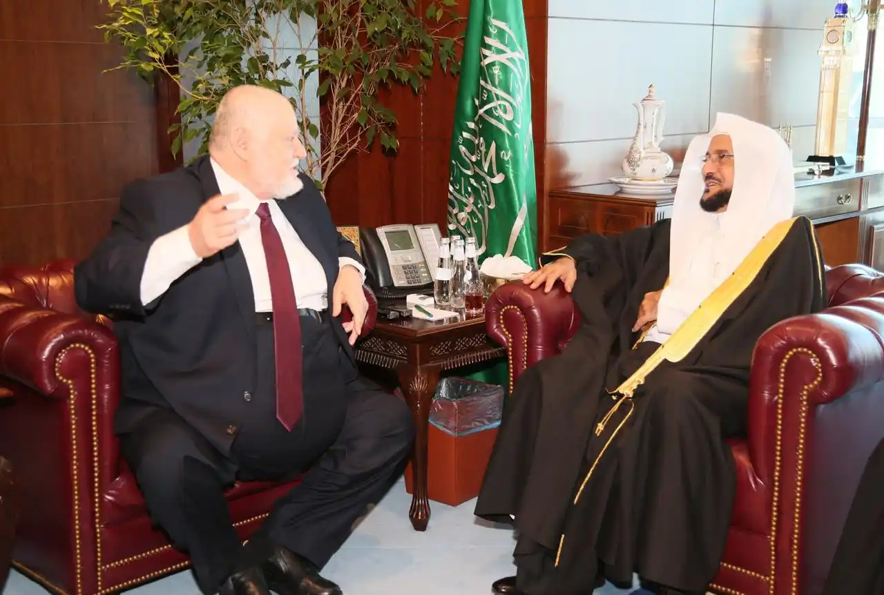 Atividades do MARKAZ - 2026 90 Representantes conversando em reunião institucional com bandeira saudita ao fundo